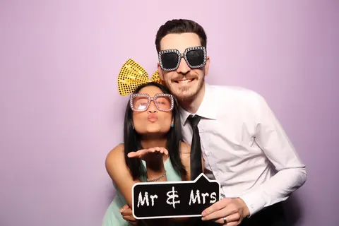 Couple posing with a Mr and Mrs sign against a pink photo booth backdrop