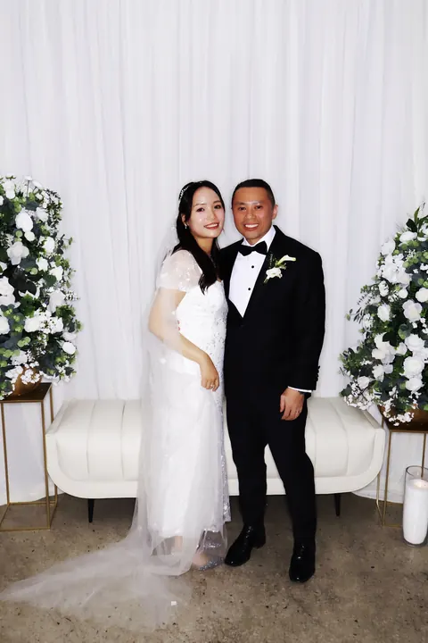 Newlyweds posing with ivory drapes, white florals and lounge seating