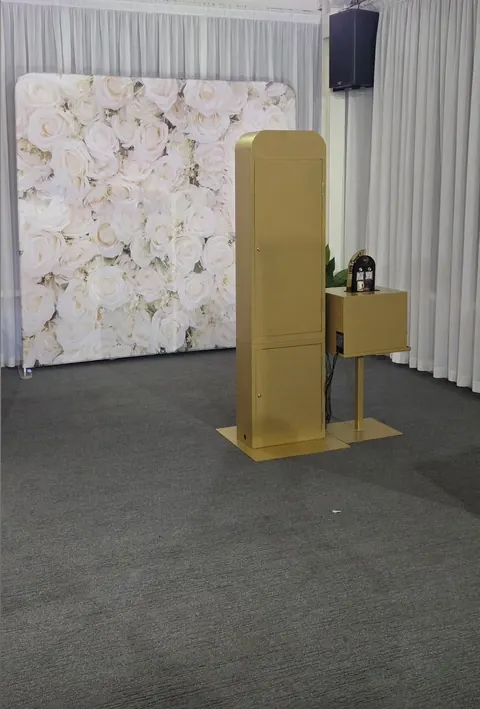 Gold Photo Booth and printer stand beside a white floral backdrop