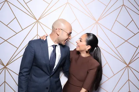 Couple posing against a white and gold geometric photo booth backdrop