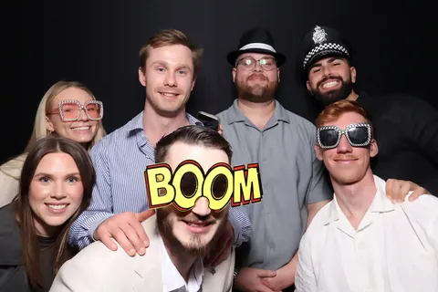 Guests posing with novelty glasses and a BOOM prop against a black backdrop