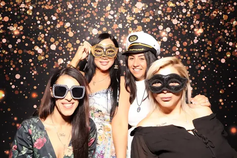 Guests wearing playful props against a sparkling photo booth backdrop