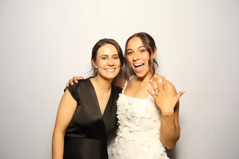 Two guests smiling in front of a white photo booth backdrop