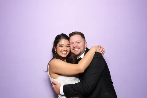 Bride and groom embracing in front of a lilac backdrop
