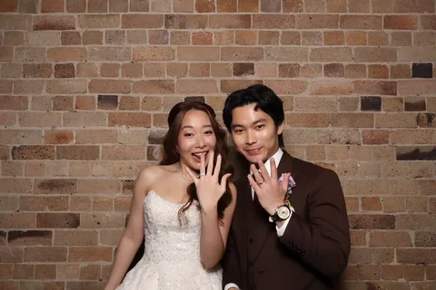 Bride and groom showing their rings in front of a brick wall