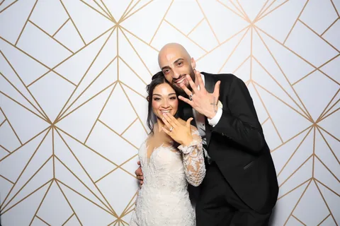 Bride and groom showing their rings against a gold geometric backdrop